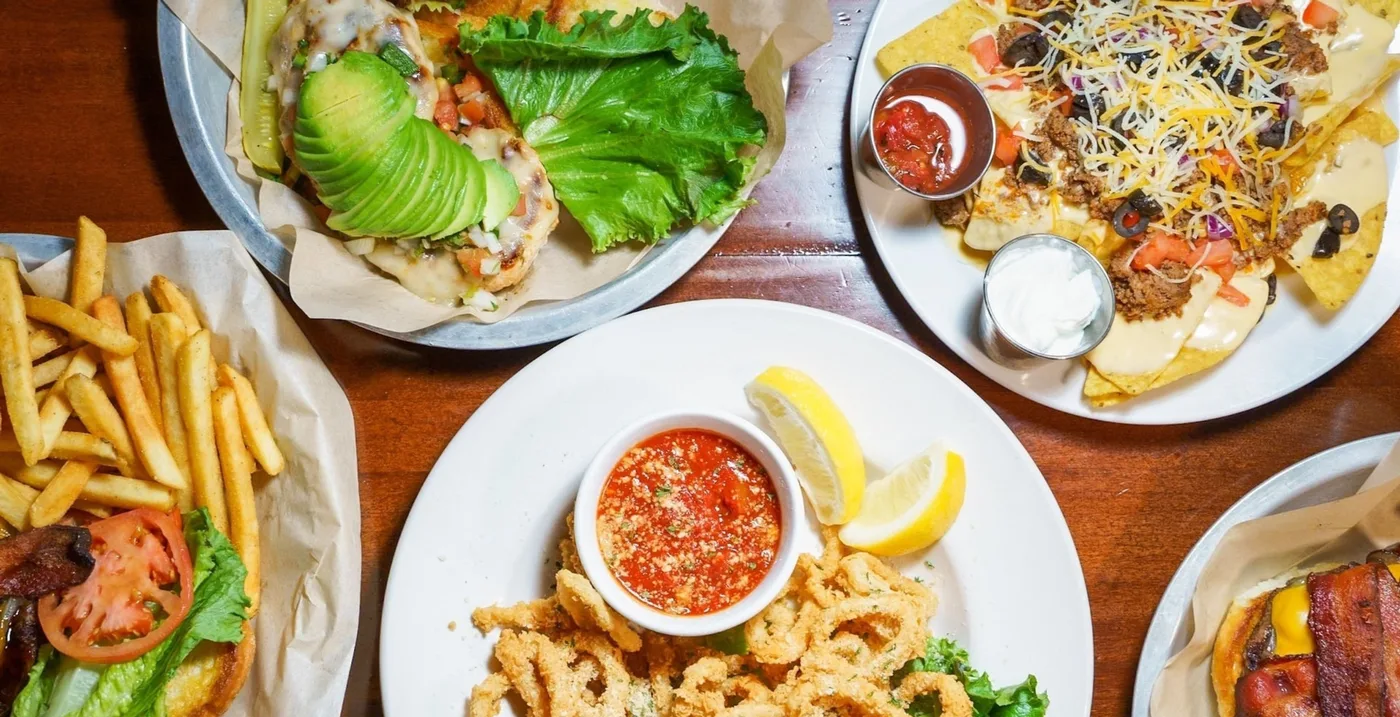 A spread of Jugs Pub and Grill food: Baja chicken sandwich, nachos, calamari and a burger
